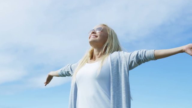 Beautiful Young Woman with Long Blonde Hair with Arms Wide Open to Celebrate Her Success and Warm Weather. Sun is Shining and Sky is Blue. Shot on RED EPIC-W 8K Helium Cinema Camera.