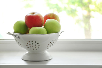Colander with fresh apples on windowsill