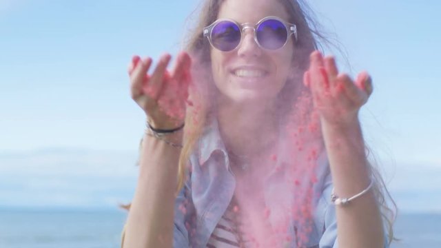Beautiful Young Young Girl with Brown Hair and In Cool Sunglasses Blows Holi Colorful Powder Off Her Hands and Laughs. Clear Blue Sky Behind Her. Shot on RED EPIC-W 8K Helium Cinema Camera.