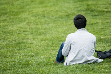 The young guy sits on the grass alone. The guy sits alone and stares into the distance. Place for text.