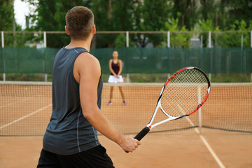 Young man and woman playing tennis on court