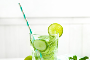 Delicious refreshing water with cucumber in glass on light background