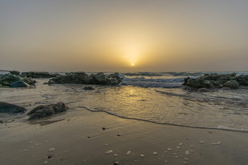 sunrise on a beach with waves and stones in the water