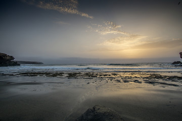 sunrise on a beach with waves and stones in the water