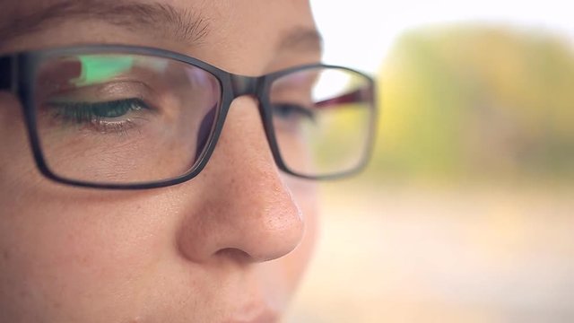 beautiful girl with glasses with blue eyes and brown hair smiles and writes a message on the phone sitting in the car
