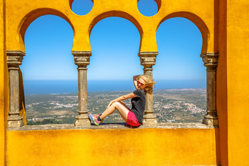Happy blonde woman sitting on arabic arches of Pena National Palace on top of a hill above...