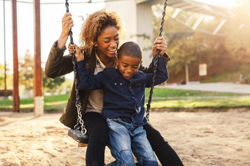Black mother and her son having fun on playground swing.