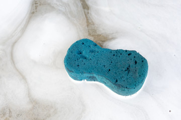 Blue sponge on an abstract white foam flow with water on dirty concrete