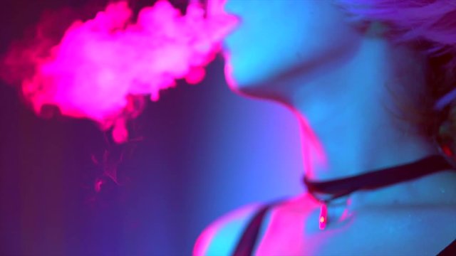 Beauty smoking girl in bright lights with colorful smoke. Woman inhaling from an electronic cigarette. Slow motion 4K UHD video 3840x2160