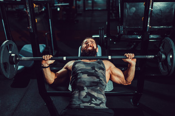 Very Strong bearded man doing bench press workout in gym