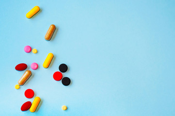 A lot of different colorful capsules and dragees with medicines. On blue background. The concept of medicine.