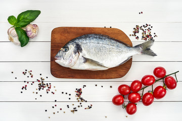 Fresh dorado fish on wooden cutting board with garlic, tomatoes and peppercorns. Top view, copy space