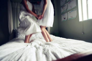 Two Girl in White Dresses Jumping on Bed