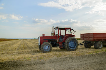 one old tractor with a trailer standing in a field during harvesting, a rural landscape