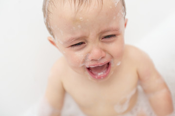 Crying baby by in a bathtub. Infant kid sreaming while taking a bath.