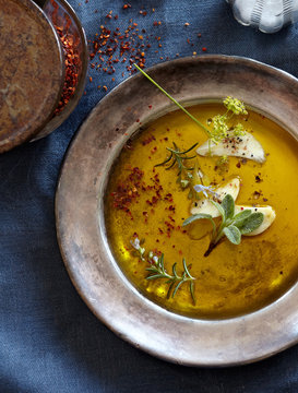 Pewter Bowl of olive oil and fresh and dried spices overhead on blue tablecloth