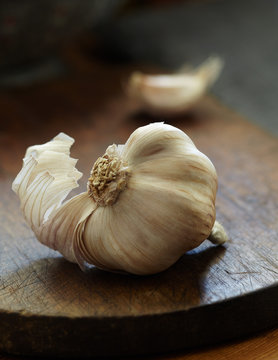 Bulb of garlic resting on cutting board with tear of garlic skin visiable