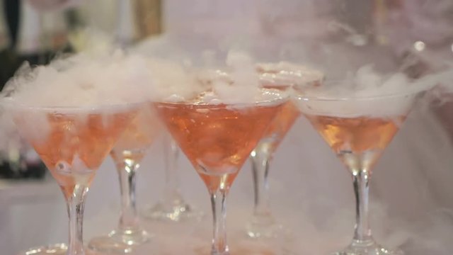 Feast alcohol. Close-up of shelf of glasses with seething wine with dry ice