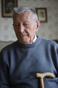 Portrait of a gray haired senior sitting alone holding a wooden cane