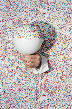 Surreal photo of a hand coming through a confetti wall, holding a balloon half covered with confetti