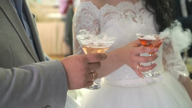 Unknown bride and groom holding goblets with seething wine with dry ice. Feast alcohol