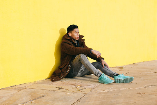 Side view of an asian man sitting in front of a yellow wall.