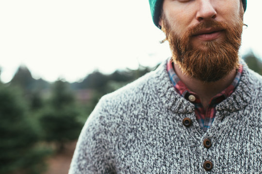 Bearded Man Wearing Green Beanie And Wool Sweater Over Red Flannel At Christmas Tree Farm