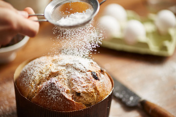 Man's hand powdering panettone with sugar using sifter