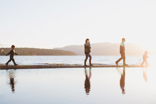 Young family of five walking along the ocean beach at sunset