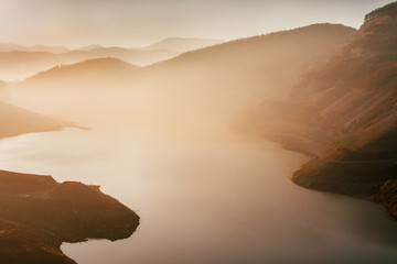 Beautiful sunset above the lake and mountains covered with light fog