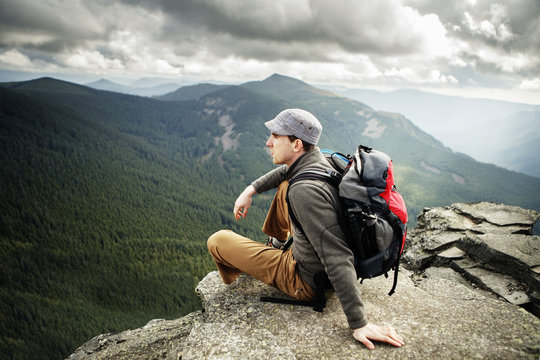 Man sitting on cliff up high overlooking forests