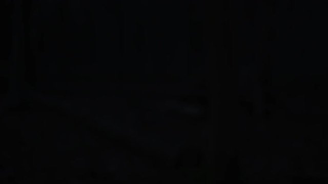Group running in the woods at night wearing lamps on headgear, woman stops to check her smartwatch.