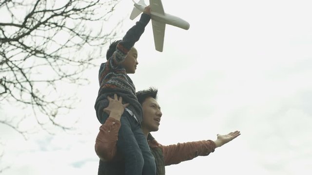Happy father carrying son on shoulders, playing outdoors with model airplane