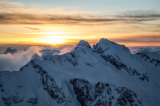 Dreamy aerial landscape view of the beautiful snow covered mountains during a cloudy sunset. Picture taken of Tentalus Range near Squamish, British Columbia, Canada.