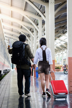 Woman and man hold hands walk in train station go travel drag bag red color,man holding map