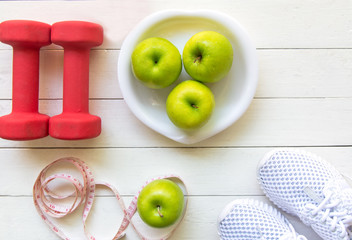 Healthy lifestyle for women diet with sport equipment, sneakers, measuring tape, fruit healthy green apples and bottle of water on wooden.  Healthy Concept.