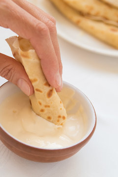 Female hand dipping pancake roll into sour cream, close-up.