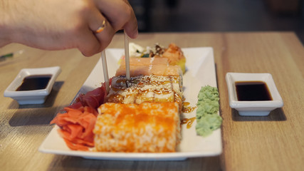 Man eating sushi and dip in sauce in sushi bar, close up