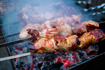 Grilled kebab cooking on metal skewers (grill). Roasted meat cooked at barbecue with smoke. Close up BBQ fresh pork meat chop slices. Traditional eastern dish, shish kebab