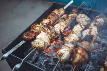 Grilled kebab cooking on metal skewers (grill). Roasted meat cooked at barbecue with smoke. Close up BBQ fresh pork meat chop slices. Traditional eastern dish, shish kebab.