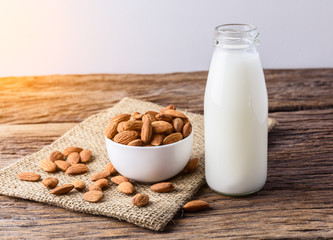 Peeled almonds with bowl and Bottle of almond milk on rustic wooden