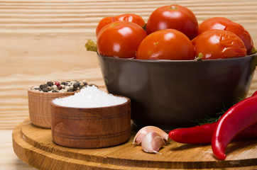 on a wooden table, there is a plate with salted red tomatoes and spices