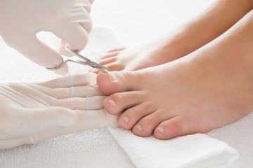 Obraz na płótnie Canvas Hands in gloves cares about a woman's foot nails. Pedicure, manicure beauty salon concept. Foot fingernails cutting with scissors.