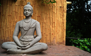 Statue of Buddhist God Buddha in sitting and meditating pose in a park 