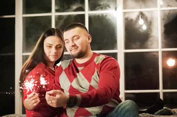 Christmas wall decor in a room in Loft style. A loving couple celebrates Christmas together. Lovers embrace on a loft bed. Hand holding lit Bengal lights