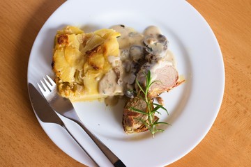 Tenderloin chops with mushroom sauce and roasted potatoes. Top down view on served dish on plain white plate and neutral wooden table
