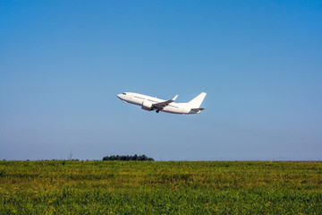 Green field, blue sky and white passenger plane takes off