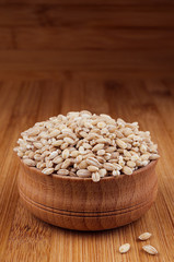 Pearl barley in wooden bowl on brown bamboo board, closeup. Rustic style, healthy dietary groats  background.