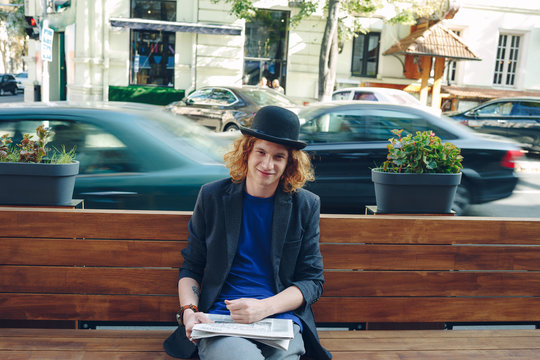 Red haired hipster man sitting on bench with newspaper
