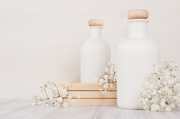 Fototapeta na wymiar Blank white cosmetics bottles with small flowers on white wood board, copy space, mock up. Soft elegant home decor for advertising, designers, branding identity, cover.